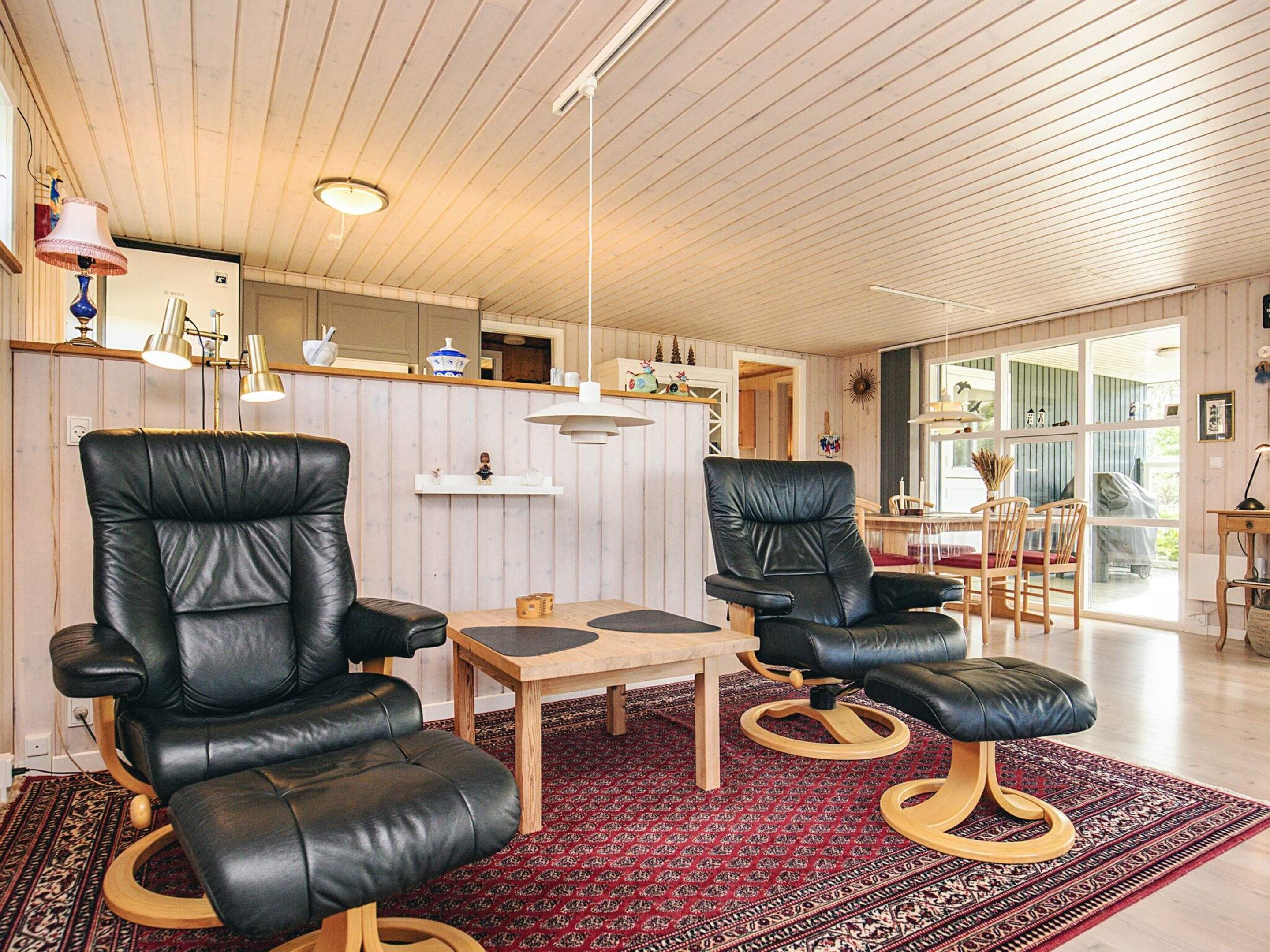 A room with two black leather chairs, a wooden table, and a patterned rug.