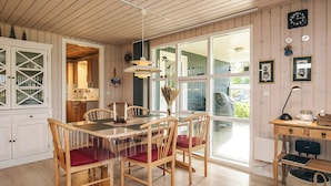 A wooden-paneled room with a dining table, chairs, and a desk with a lamp.