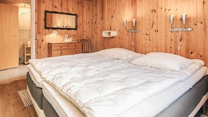A bedroom with a wooden ceiling and walls, a bed with white bedding, a dresser, a mirror, and wall-mounted lights.