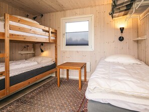 Une chambre avec deux lits superposés, un lit simple, une petite table en bois, un tapis à motifs et une fenêtre avec des stores.