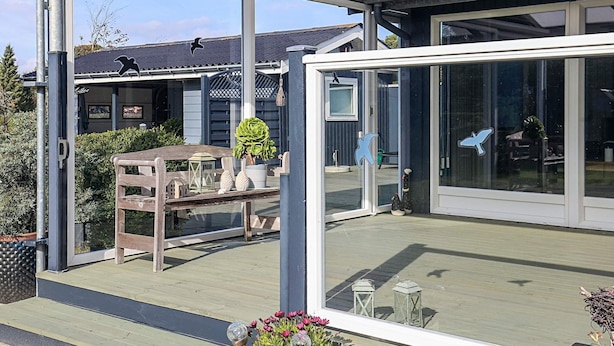 A covered outdoor area with a wooden deck, a glass door, and a view of a building with a dark roof and a bird logo.