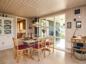 Un coin repas avec une table et des chaises en bois, une cuisine à l’arrière-plan et une grande fenêtre donnant sur un beau paysage.