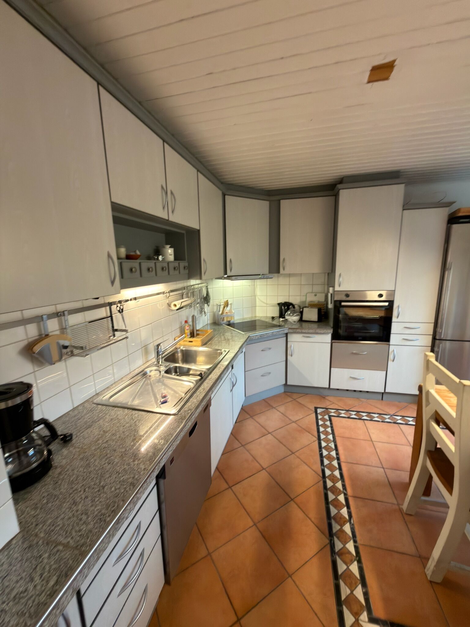 A compact kitchen with white cabinets, a built-in oven, a sink, and a coffee maker.