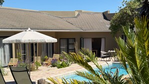 A pool area with lounge chairs and an umbrella, surrounded by greenery and a building with a tiled roof. - Kokon Boutique Guesthouse (Cape Town)
