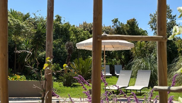 A garden with a pergola, two lounge chairs, and a large umbrella. - Kokon Boutique Guesthouse (Cape Town)