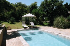 A swimming pool with two lounge chairs and a patio umbrella.