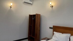 A hotel room with a bed, a wooden wardrobe, two wall-mounted lights, and an air conditioning unit. - La Million Palace (Dodoma)