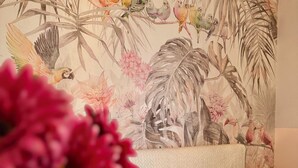 Un dormitorio con cama, mesita de noche, lámpara y un mural floral en la pared.