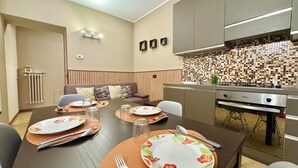 Un comedor moderno con una mesa de madera dispuesta para cuatro personas, una cocina con salpicadero de azulejos y una estufa empotrada.