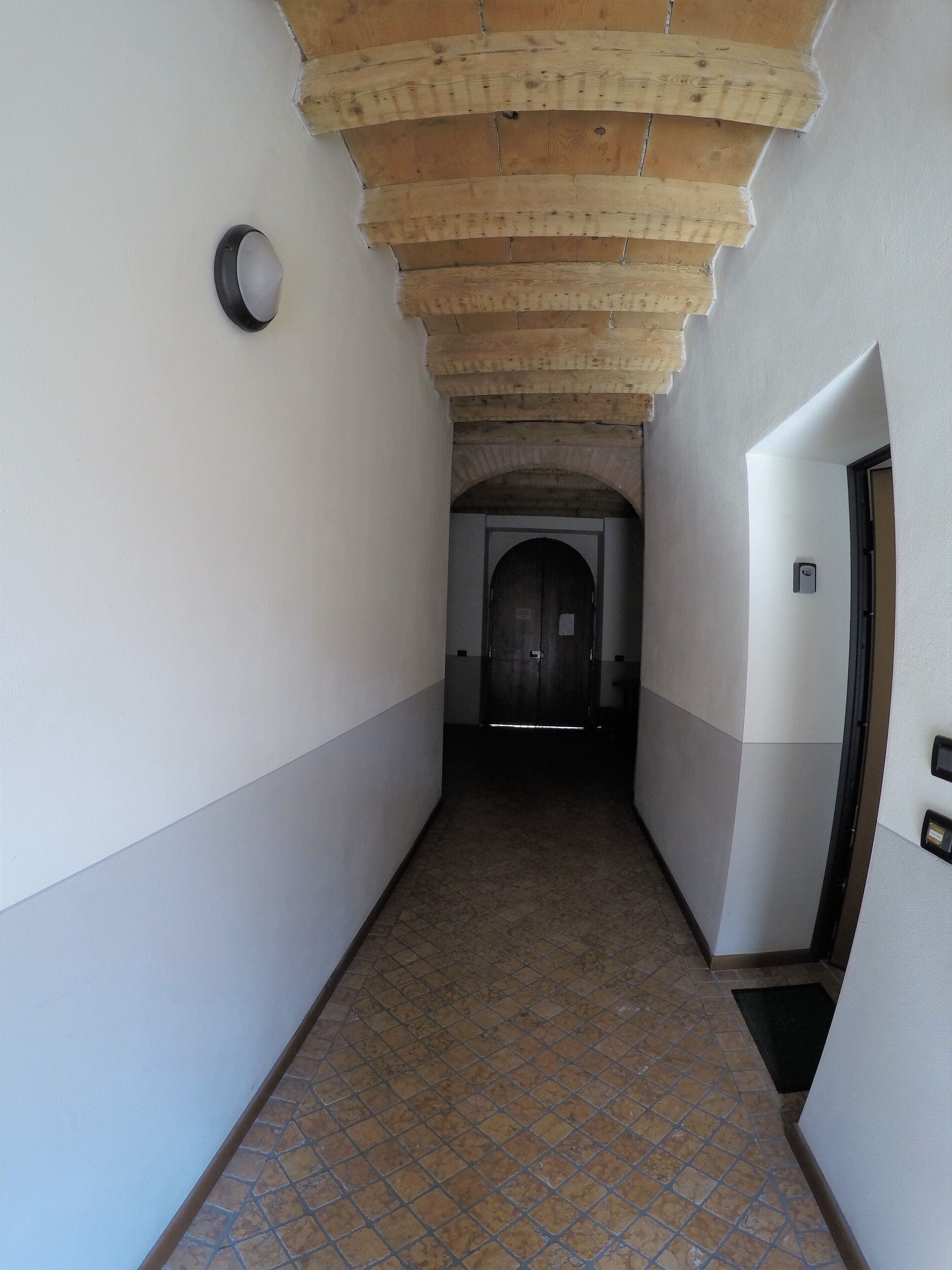 Un couloir avec un sol carrelé, un plafond en bois et une porte au fond.