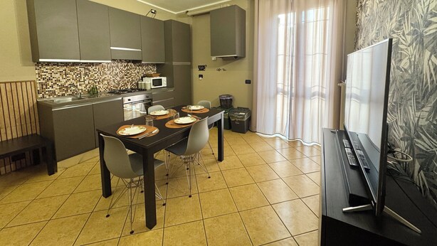 Una cocina moderna con una mesa de comedor preparada para cuatro personas, microondas y un amplio ventanal con cortinas.