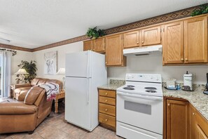 A kitchen with wooden cabinets, a white refrigerator, a stove, and a dining area with a leather couch.