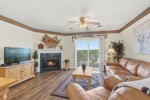 Un salon avec une cheminée, un canapé en cuir, une télévision et un ventilateur de plafond.