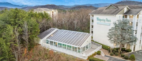 Un edificio moderno con un amplio frente de vidrio y paneles solares, rodeado de un bosque denso y montañas.
