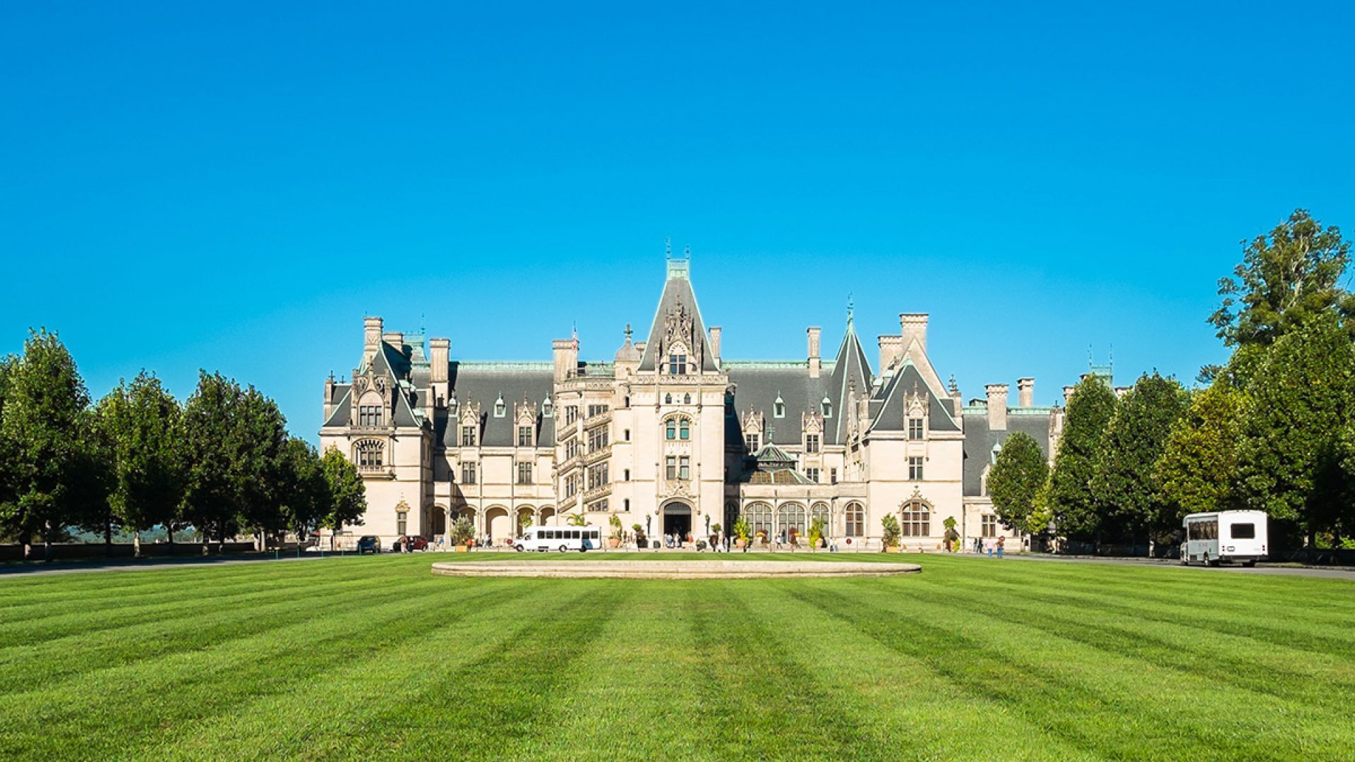Un grand bâtiment historique à la façade symétrique, doté d’une tour centrale et d’une pelouse bien entretenue à l’avant.