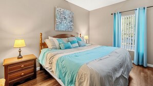 A bedroom with a bed, nightstands, a painting, and a window with curtains.