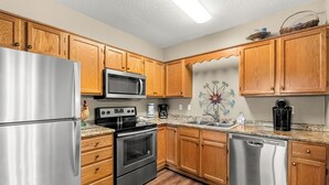 A kitchen with wooden cabinets, stainless steel appliances, a microwave, stove, dishwasher, and a decorative wall piece.