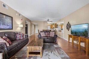 Ein Wohnzimmer mit Sofa, Couchtisch, Fernseher und einem Essbereich im Hintergrund.