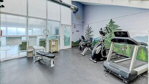 A gym with exercise equipment, large windows, and a mural of a forest. - Two bedroom, two bath condo| Pigeon Forge| City View (Pigeon Forge)