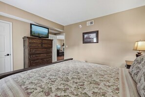 A bedroom with a bed, dresser, television, and a lamp.