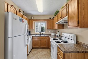 A kitchen with wooden cabinets, a white refrigerator, a stove, and a window with blinds.