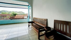 Un balcon avec un banc en bois et un bol, un sol carrelé et une vue sur la verdure et les collines.