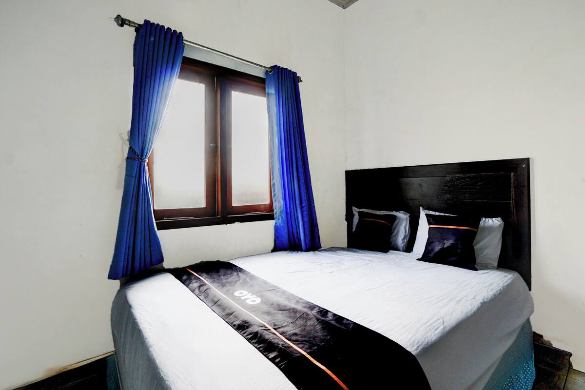 A bed with a black and white bedspread, a window with blue curtains, and a wooden headboard.
