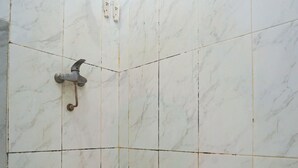 Une salle de bain avec des carreaux de marbre blanc, une douche équipée d’un pommeau de douche à main et une prise électrique visible sur le mur.