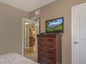 A bedroom with a bed, a dresser, and a television on the wall.