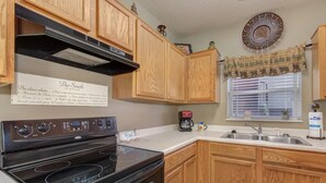 A kitchen with wooden cabinets, a black stove, a coffee maker, and a window with blinds. - Three bedroom, three bath condo| Pigeon Forge| Close to Dollywood| Sleeps 8 (Pigeon Forge)