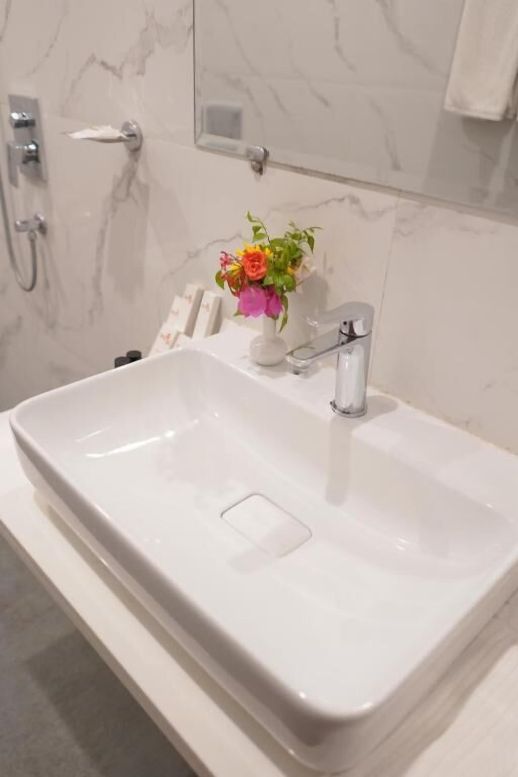 Un baño con lavamanos blanco, espejo y toallero.