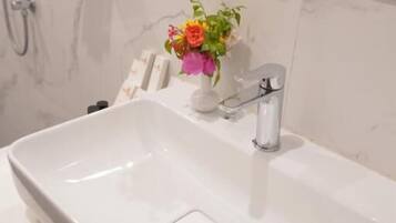 Un baño con lavamanos blanco, espejo y toallero.