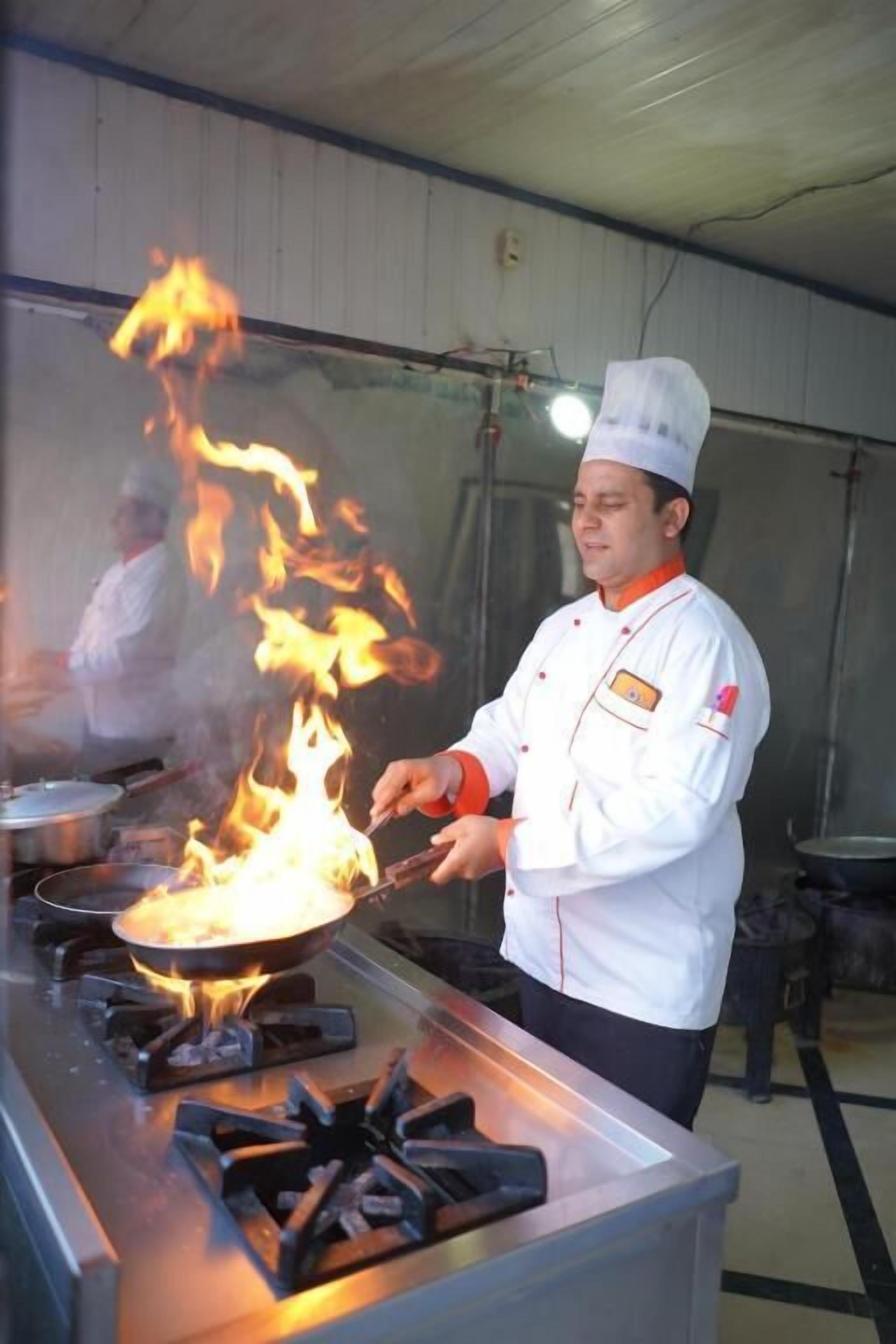 Un chef cuisinant au-dessus d’une flamme sur une cuisinière dans une cuisine.