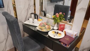 Hotelkamer met een marmeren wand, een zwart bureau, een stoel, een koffiezetapparaat, een bord met eten, een vaas met bloemen en een boek.