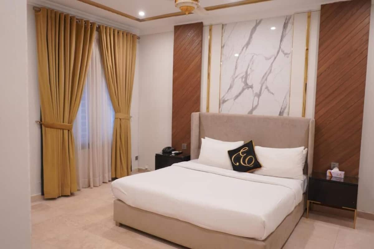 Ein Schlafzimmer mit einem großen Bett, einem Nachttisch, einer Wand mit Marmormuster und Vorhängen.