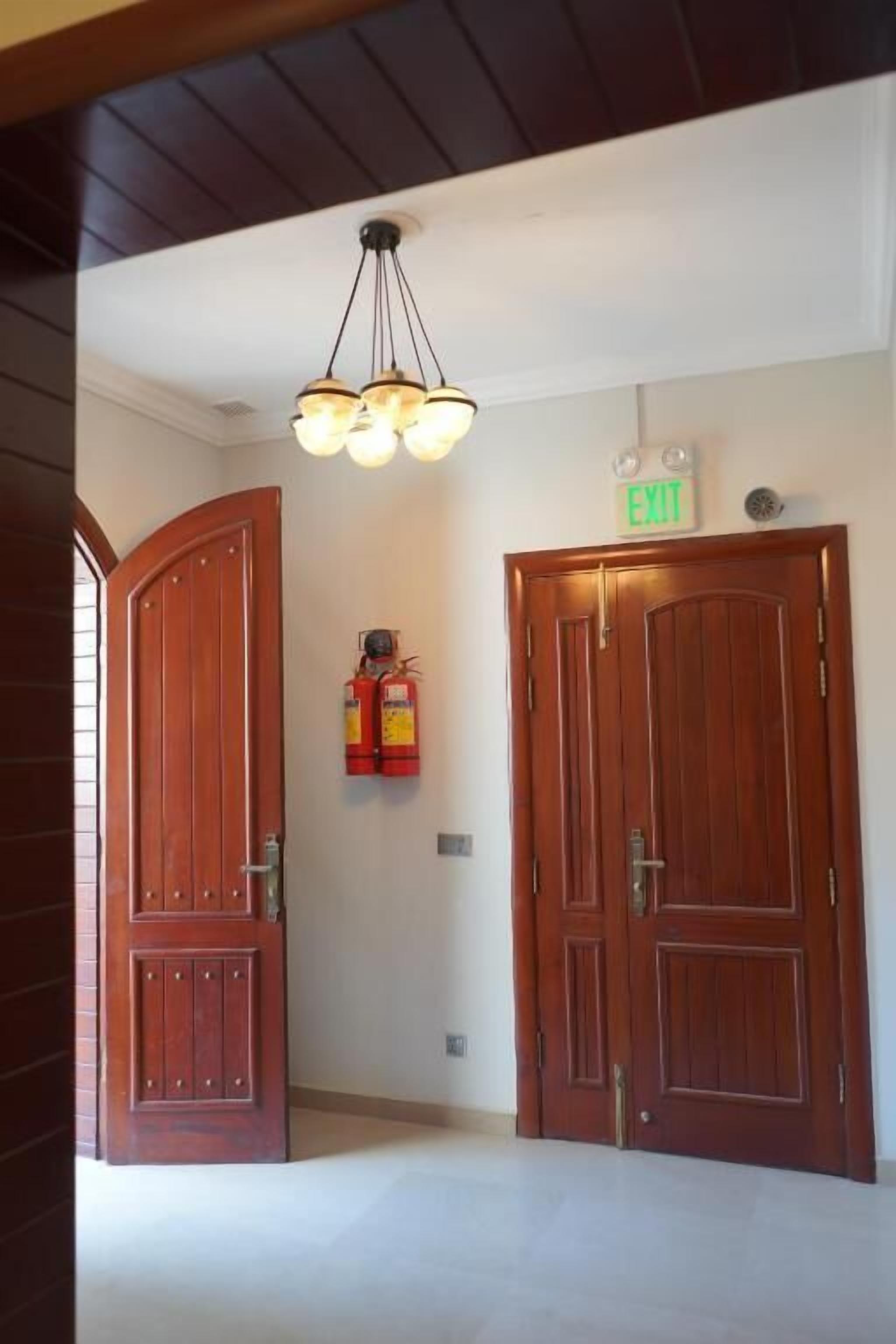 Un pasillo con dos puertas de madera, un letrero de salida y una lámpara en el techo.