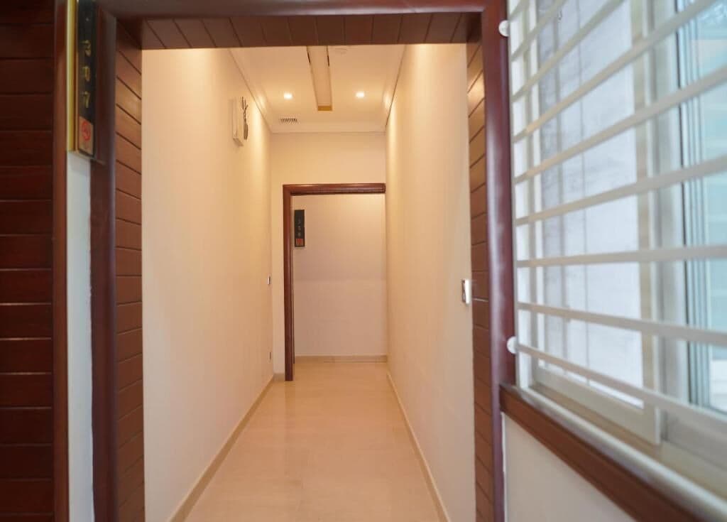 A narrow hallway with a wooden door at the end, leading to a room with a window.