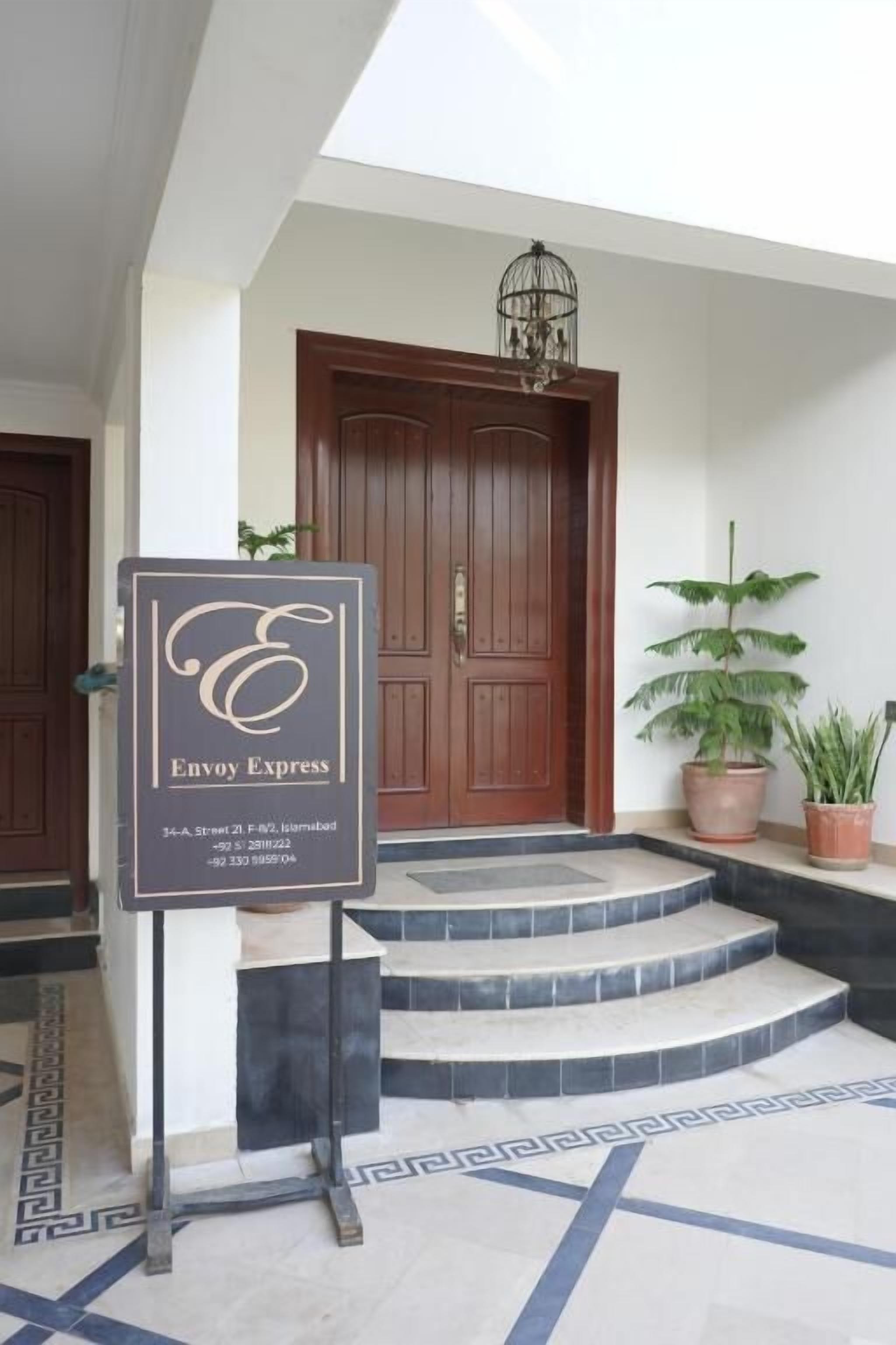 L’entrée d’un hôtel, avec une enseigne indiquant « Envy Express », une porte en bois et un escalier menant à l’entrée.