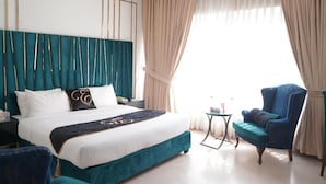 Een hotelkamer met een groot bed, een blauwe fauteuil, een kleine tafel en uitzicht op de omgeving.