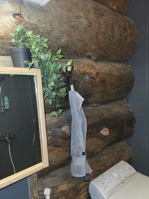 Ein Badezimmer mit einer Wand aus Holzstämmen, einer Topfpflanze, einem Handtuchhalter und einer weißen Toilette.
