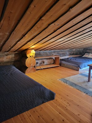 Ein gemütliches Schlafzimmer im Dachgeschoss mit Holzbalkendecke, einem Bett mit blauer Steppdecke, einem kleinen Holztisch und einer Lampe.