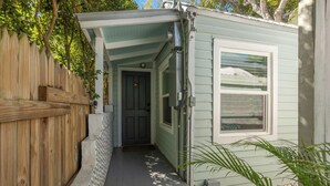 Una piccola struttura in legno verde chiaro con una porta e una finestra, una recinzione in legno e un piccolo portico.
