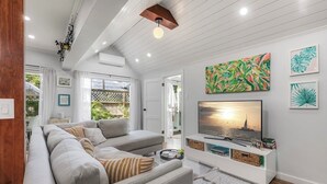 Un soggiorno moderno con un divano componibile, una televisione a schermo piatto e opere d'arte a tema tropicale.