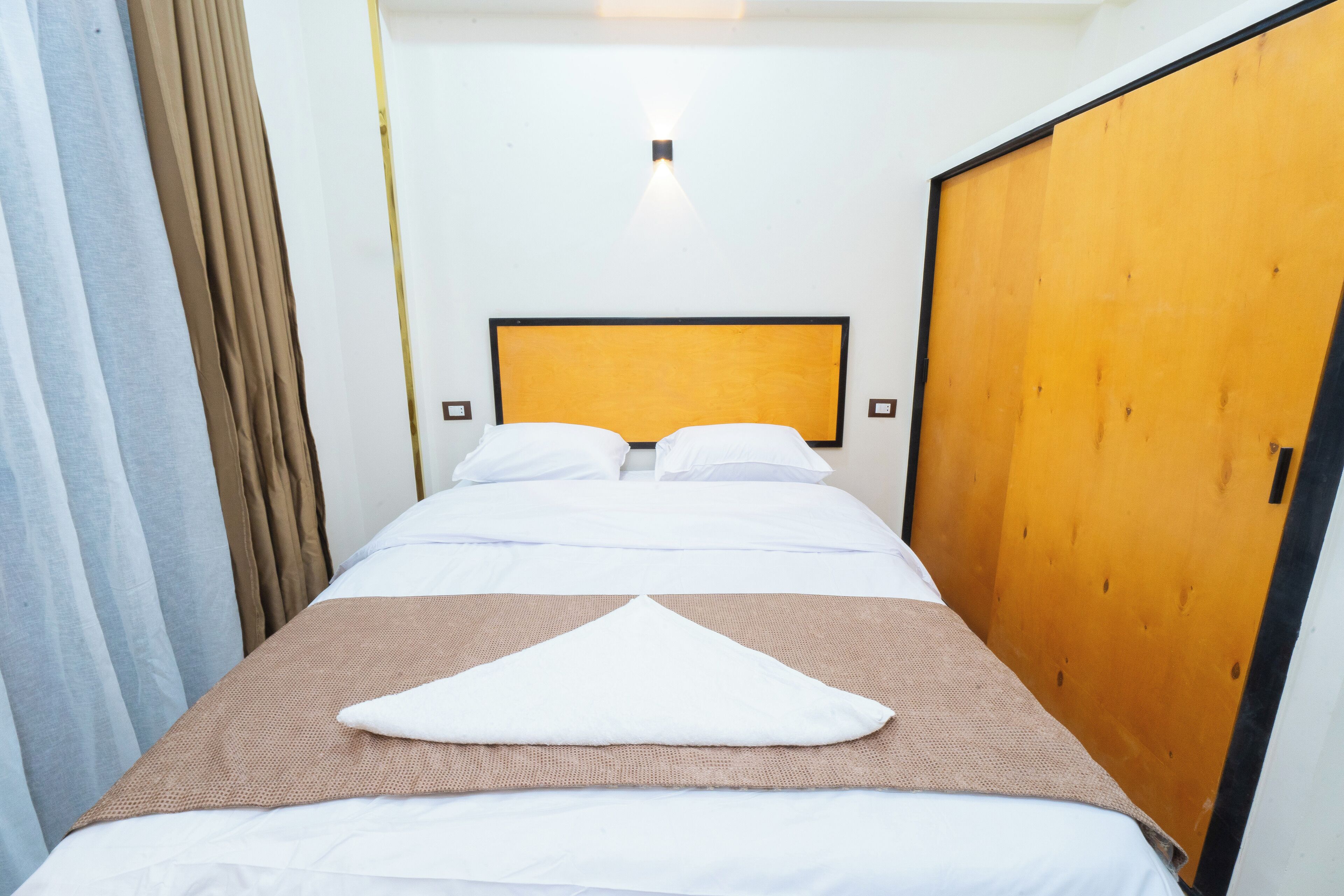 A hotel room with a bed, a wooden wardrobe, and a curtain.