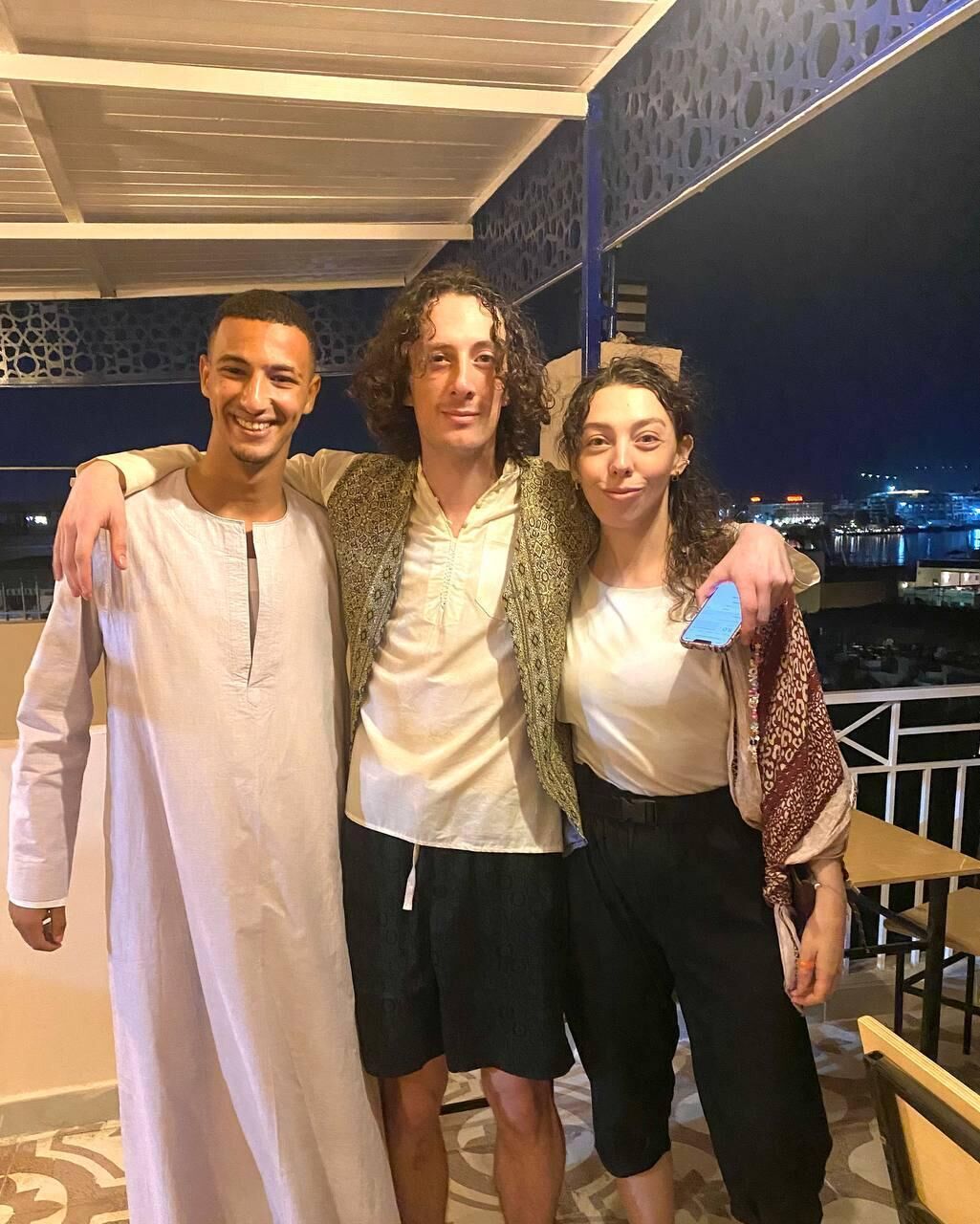 Three people standing together in an indoor setting with a cityscape view in the background.