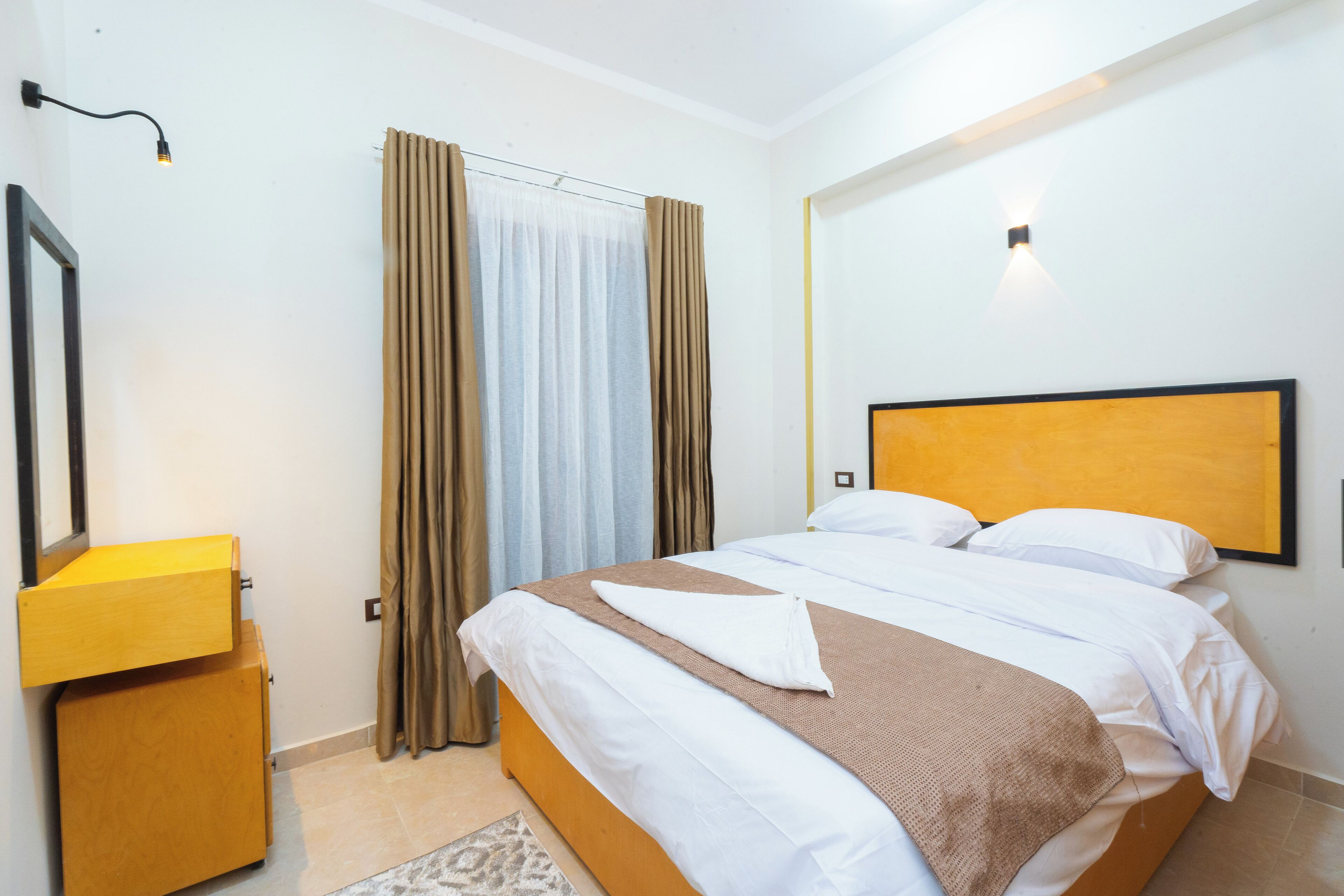 A neatly made bed with white and brown linens, a wooden headboard, and a bedside table with a lamp.