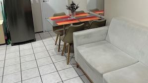 Ein Zimmer mit einem weißen Sofa, einem Esstisch mit Stühlen, einem Kühlschrank, einer Tür mit einem Schild und einem Spiegel an der Wand.