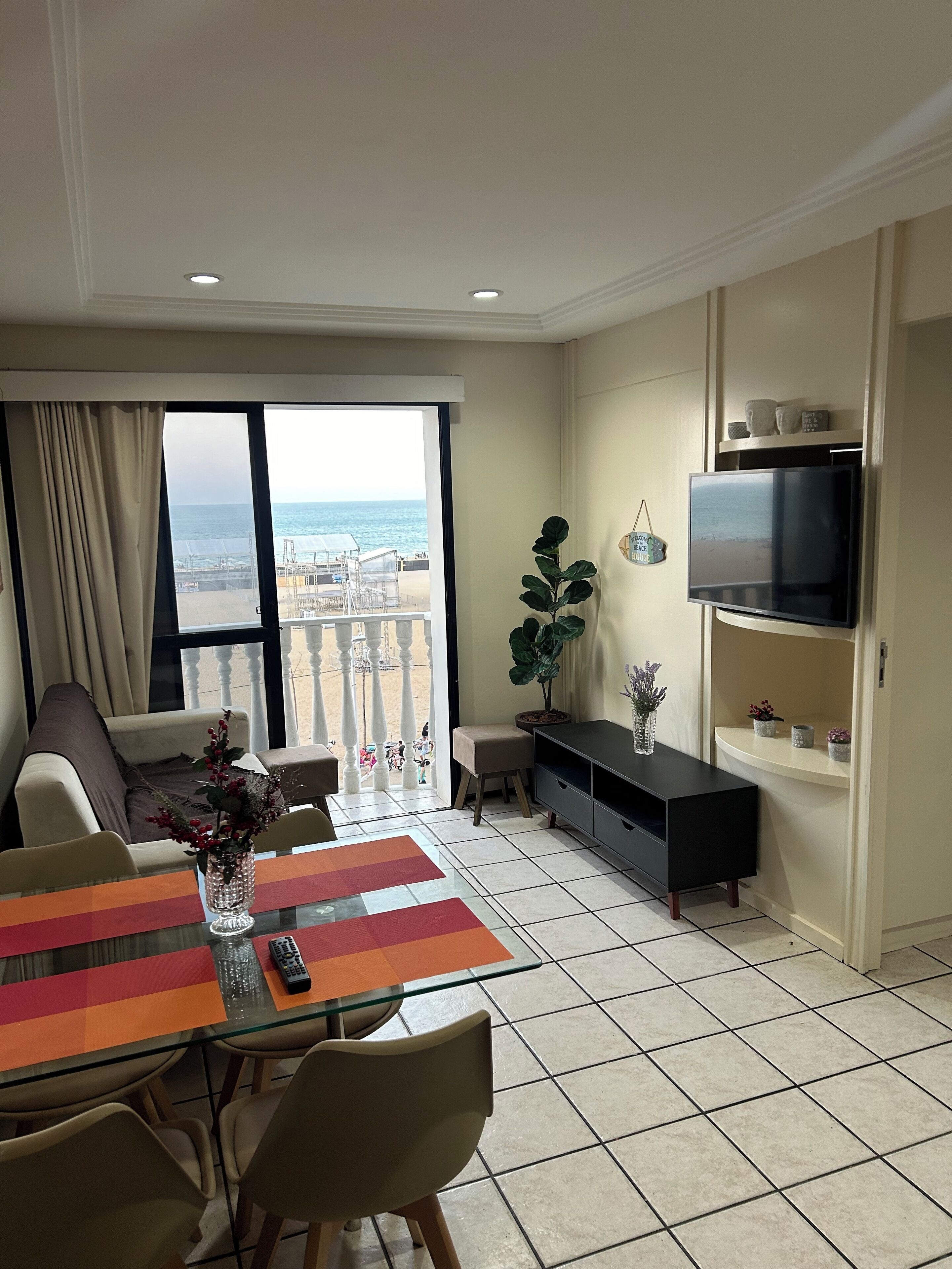 Uma sala de estar moderna com varanda, uma TV na parede e um espaço de jantar com mesa e cadeiras.