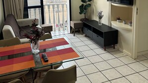 Ein modernes Wohnzimmer mit Balkon, einem an der Wand befestigten Fernseher und einem Essbereich mit Tisch und Stühlen.