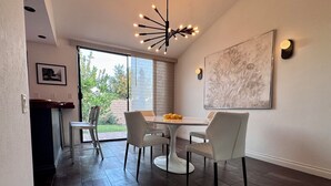 Un comedor moderno con puerta de vidrio que da a un patio, una lámpara contemporánea y un cuadro abstracto grande en la pared.